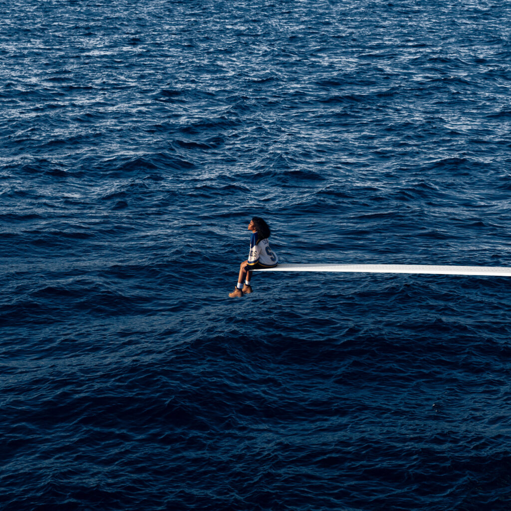SZA seated on a diving board above the ocean on the SOS album cover